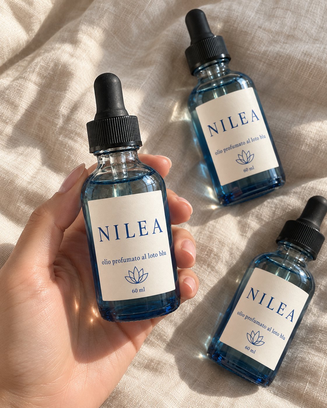 Una mano tiene una boccetta Nilea da 60 ml in vetro blu; altre due sono appoggiate su un lenzuolo di lino.